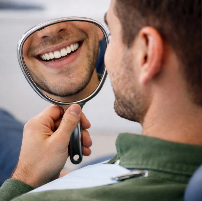 Homme admirant son sourire dans un miroir de dentiste